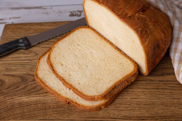 Wheat (white) bread with a crispy crust on a wooden board, cut into slices. Homemade baking in rustic style. Selective focus, close-up.