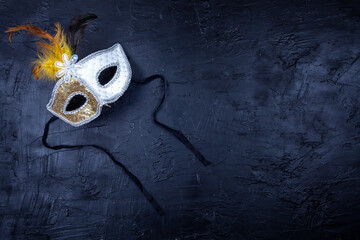 White and gold mask with feathers, isolated on a textured black background