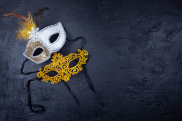 Two Venetian masks together, one golden and one white with feathers, on a black background