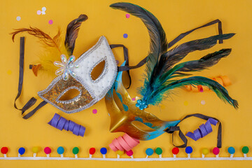 Two masks together on a yellow background, adorned with confetti and colorful streamers