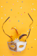 Gold and white mask with feathers, isolated on a yellow background with colorful confetti