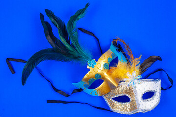 Two Venetian masks with feathers and glitter, isolated on a blue background