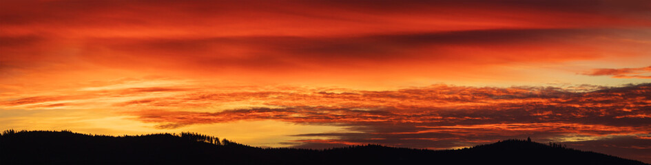 Alpenglow on sunset cloudy sky with black silhouette forest horizon. Czech panoramic landscape background