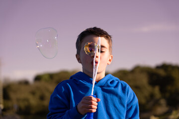 Boy blowing soap bubbles at sunset