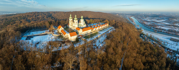 Camaldolese monastery and baroque church in the wood on the hill in Bielany, Krakow, Poland , Aerial panorama in sunset light in winter with Vistula River and far view of Cracow city in the background - 715732113