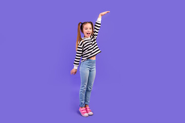 Full length photo of pretty excited small kid wear striped sweater rising arm showing height empty...