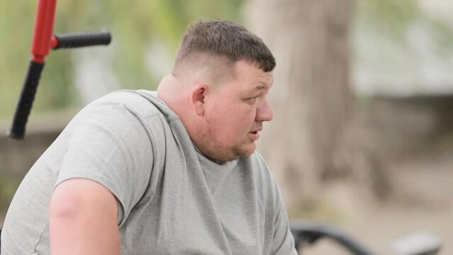 A tired fat man rests, takes a breather during training. Overweight man on outdoor exercise machine