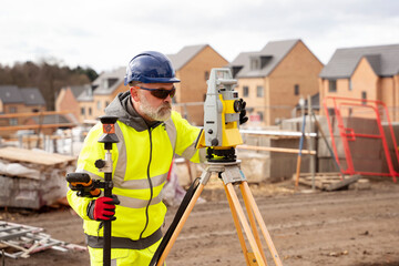 Surveyor builder site engineer with theodolite total station at construction site outdoors during surveying work - obrazy, fototapety, plakaty