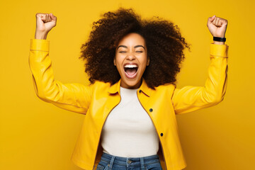 Overjoyed cheerful African American woman dressed stylish clothes celebrate success raise hands fists isolated on yellow color background