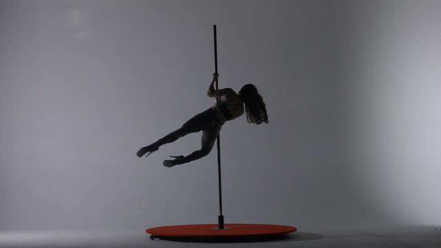 Sexy woman in leather pants and high heels spins on a dancing pole. Woman performs pylon dance in dark studio in strobe light.