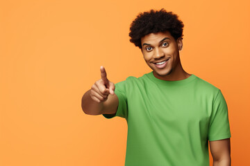 Positive excited African American guy wear green shirt looking pointing empty space isolated orange...