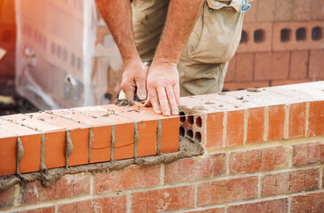 Industrial bricklayer laying bricks on cement mix on construction site close-up