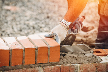 Industrial bricklayer laying bricks on cement mix on construction site close-up - obrazy, fototapety, plakaty
