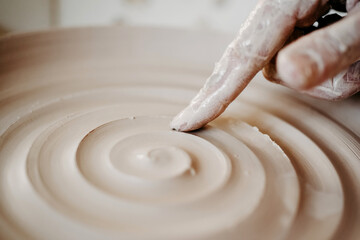 Decorating wet clay on a potter's wheel with a wine groove. A potter draws a spiral with his finger on the bottom of a white clay plate. Abstract clay background Macro