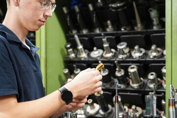 A worker inspects and selects a tap for cutting threads in parts on a CNC milling and turning...