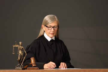 Judge working with document indoors, selective focus. Mallet and figure of Lady Justice on wooden...