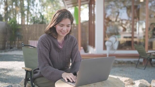 Young happy smiling Asain woman in cafe working video call facetime type project working on her laptop notebook personal computer, Female begins typing say hello on screen
