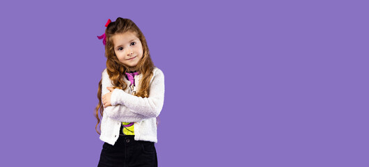 The picture of a small and beautiful girl with very fluffy and arranged hair, very stylishly dressed is posed on a purple background using the picture for advertisements and banners.