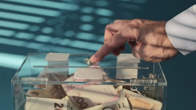 Hand give Charity in nominal 200 Ukrainian hryvnia UAH banknotes to a transparent donation box for money donation. A financial support, collects money .  giving supports charitable 