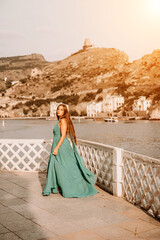 Fototapeta premium Woman sea trevel green dress. Side view a happy woman with long hair in a long mint dress posing on a beach with calm sea bokeh lights on sunny day. Girl on the nature on blue sky background.