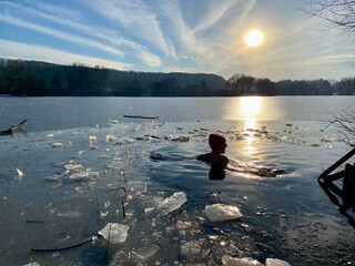Eisbaden, Frau schwimmt im Eisloch, See zugefroren. Sonnenuntergang