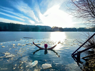 Eisbaden, Frau schwimmt im Eiswasser und hält die Arme in der Siegespose hoch, See zugefroren.