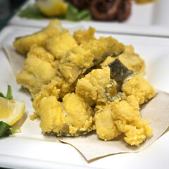 piatto di baccalà fritto servito sul tavolo di un ristorante con una fetta di limone - 715775744