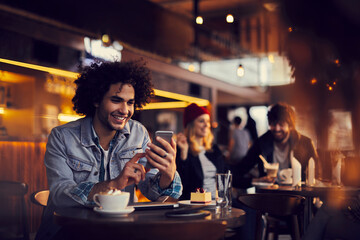 Smiling young man using smartphone in a cafe