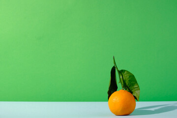 Clementine fruit with leafs against green and blue colored background