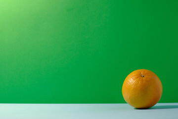Single orange fruit against green and blue colored background