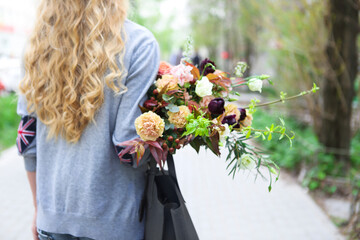 Young beautiful woman walking on the street with bag and bouquet of a flowers