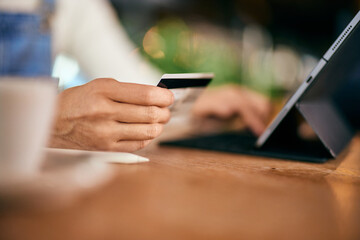 A female hand holding a credit card and using a tablet, at the cafe.