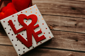 box with the word love filled with red hearts on a wooden background