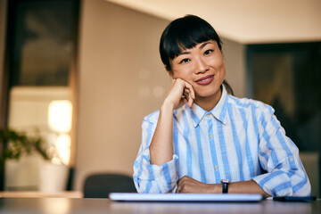 A smiling Asian businesswoman, looking at the camera while sitting at the office.