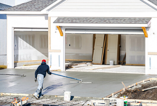 Man working on smoothing concrete driveway for the new home build at construction site. Architecture and exterior structure base progress, safety foundation pavement ground. Real estate industry.