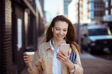 Happy woman with coffee and smartphone walking on sidewalk