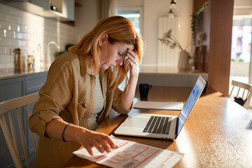 Concerned woman reviewing documents while working from her home kitchen