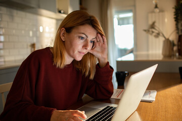 Concerned woman reviewing documents while working from her home kitchen