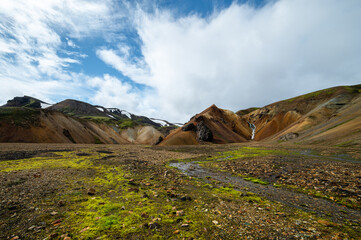 The picturesque valley in Landmannalaugar national park. Icelandic landscape of rainbow volcanic rhyolite mountains and waterfall in cloudy weather. Famous Laugavegur hiking trail. Iceland in august. 