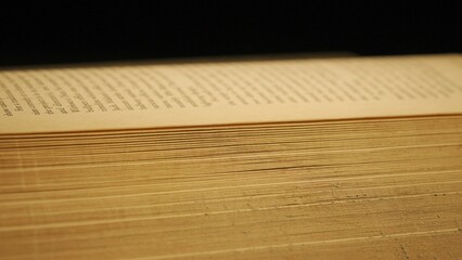 Studio shot of old retro hardcover book on dark background in warm light. Extreme close up of opened old vintage book.