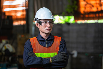 Asian man engineer industrial foreman wearing protective eyewear standing with arms crossed. technician worker in safety uniform. Industry technology manufacturing factory. looking with vision.