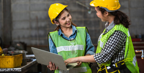 Two Asian female engineer workers wearing safety helmet discuss project in industry manufacturing....