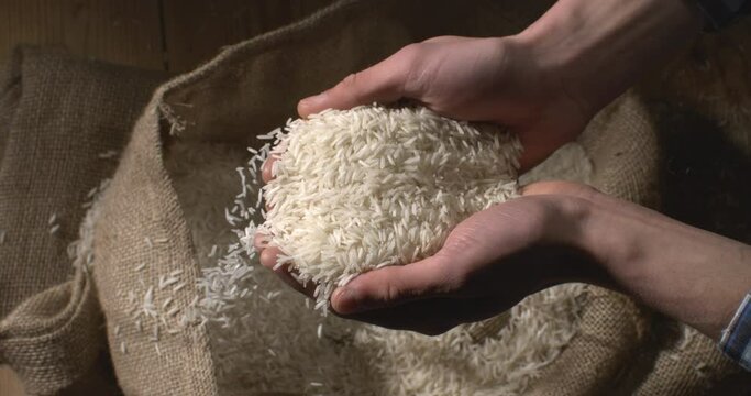 Super slow motion close up of farmer is controlling quality of handful dry basmati quality white rice over burlap sack background at 1000 fps.