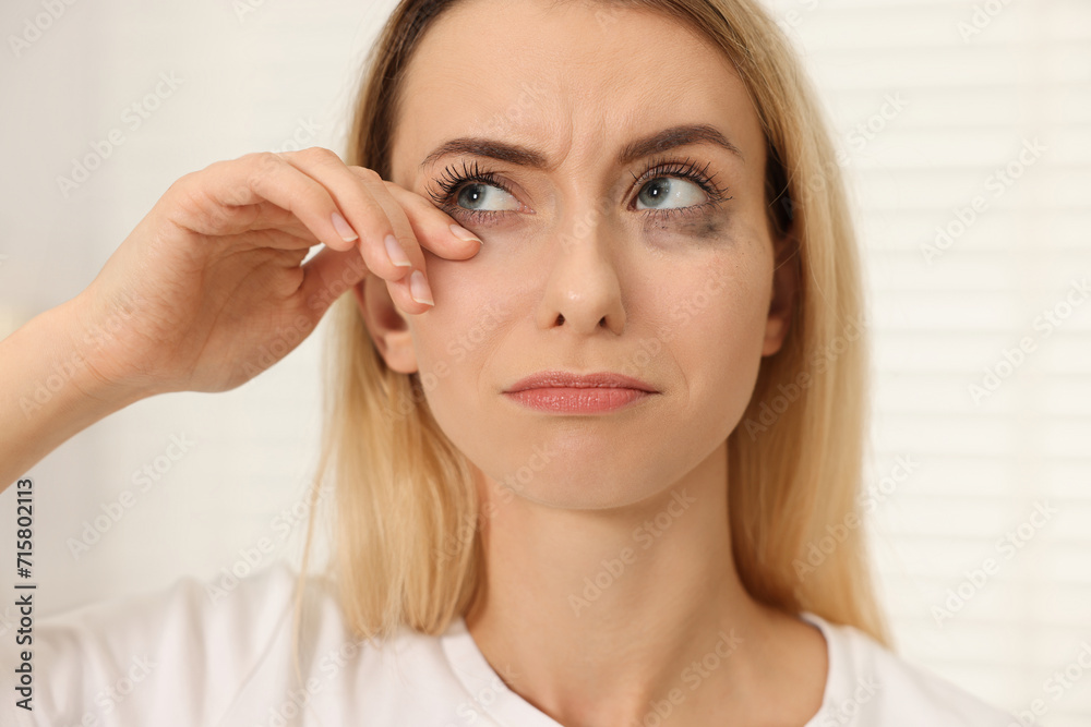 Wall mural Sad woman with smeared mascara crying indoors, closeup