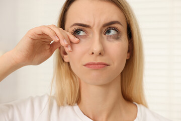 Fototapeta premium Sad woman with smeared mascara crying indoors, closeup
