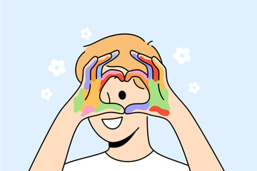 Little artist demonstrates heart gesture with hands, showing love for drawing and using watercolor. Kind boy with palms covered with paints after drawing during lessons in primary school