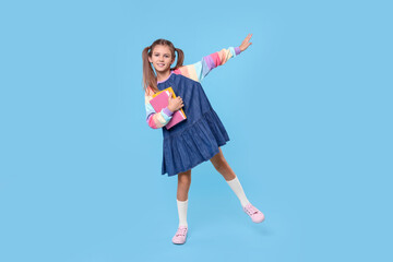 Smiling schoolgirl with books on light blue background