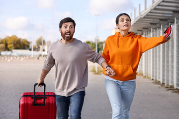 Being late. Couple with red suitcase running outdoors