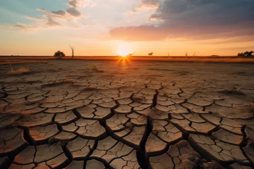 Foto auf Acrylglas The sun sets dramatically over a vast landscape of dry, cracked soil, evoking the severity of drought conditions.  © Kamonwan