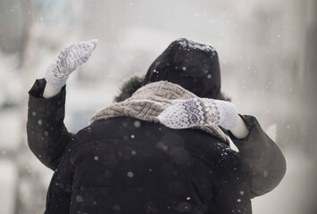 Hugging couple in love outdoors in winter. Woman hiding behind man. Cute couple kissing while covering face with a hood. Love in the street. Passionate lovers expressing their affection for each other